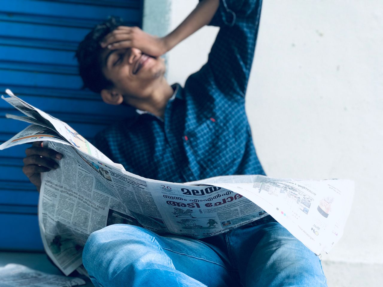 about-01 A young South Asian man casually reading a newspaper outdoors in Ernakulam, India.