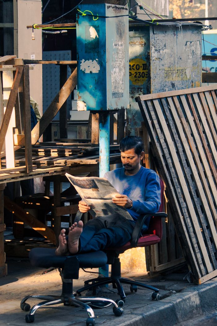 The Art of Drawing Readers In: Your attractive post title goes here Casual scene of a man reading a newspaper on a chair in an urban Mumbai street.